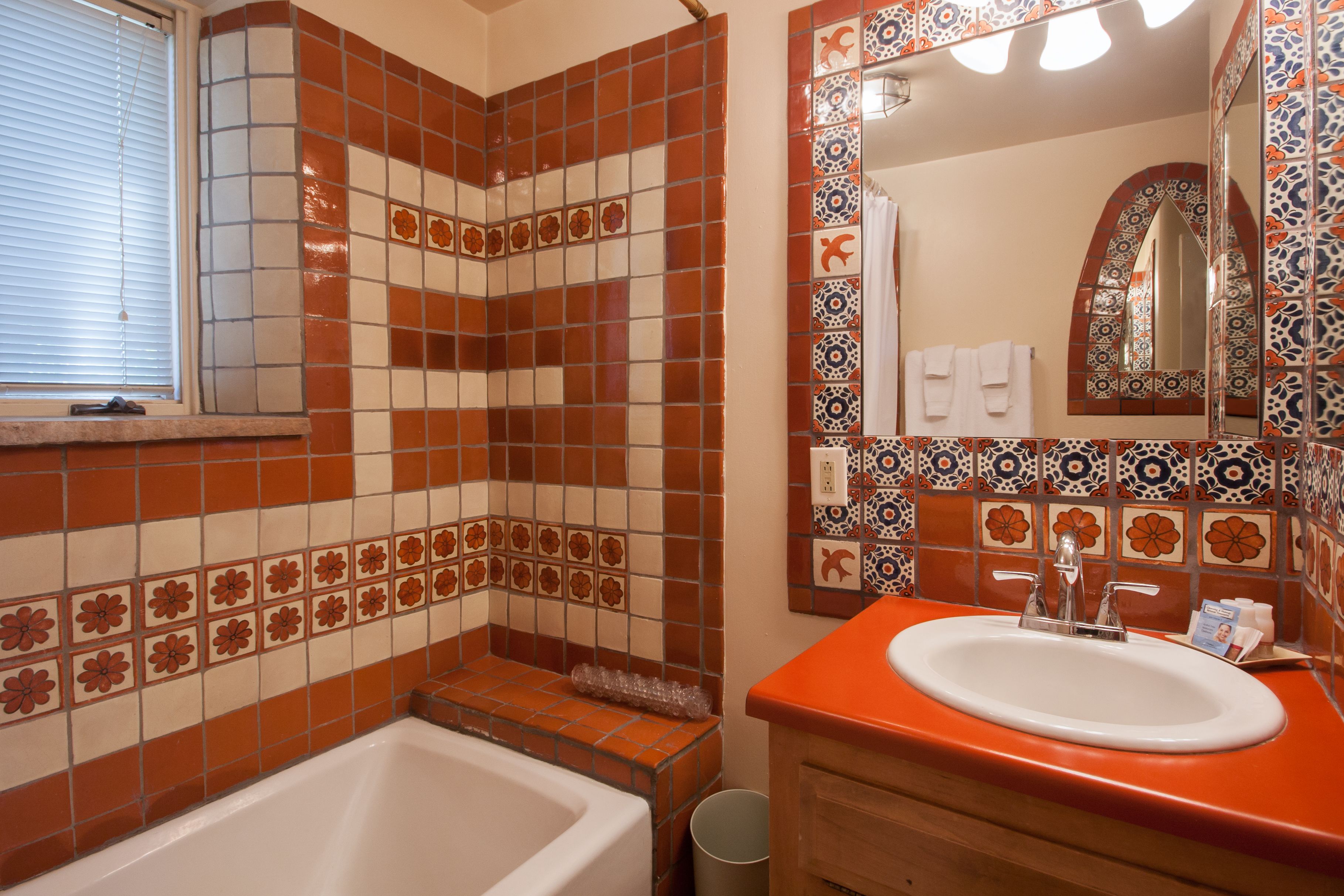 Un baño con una bañera blanca, un lavabo naranja y un espejo con marco decorativo.