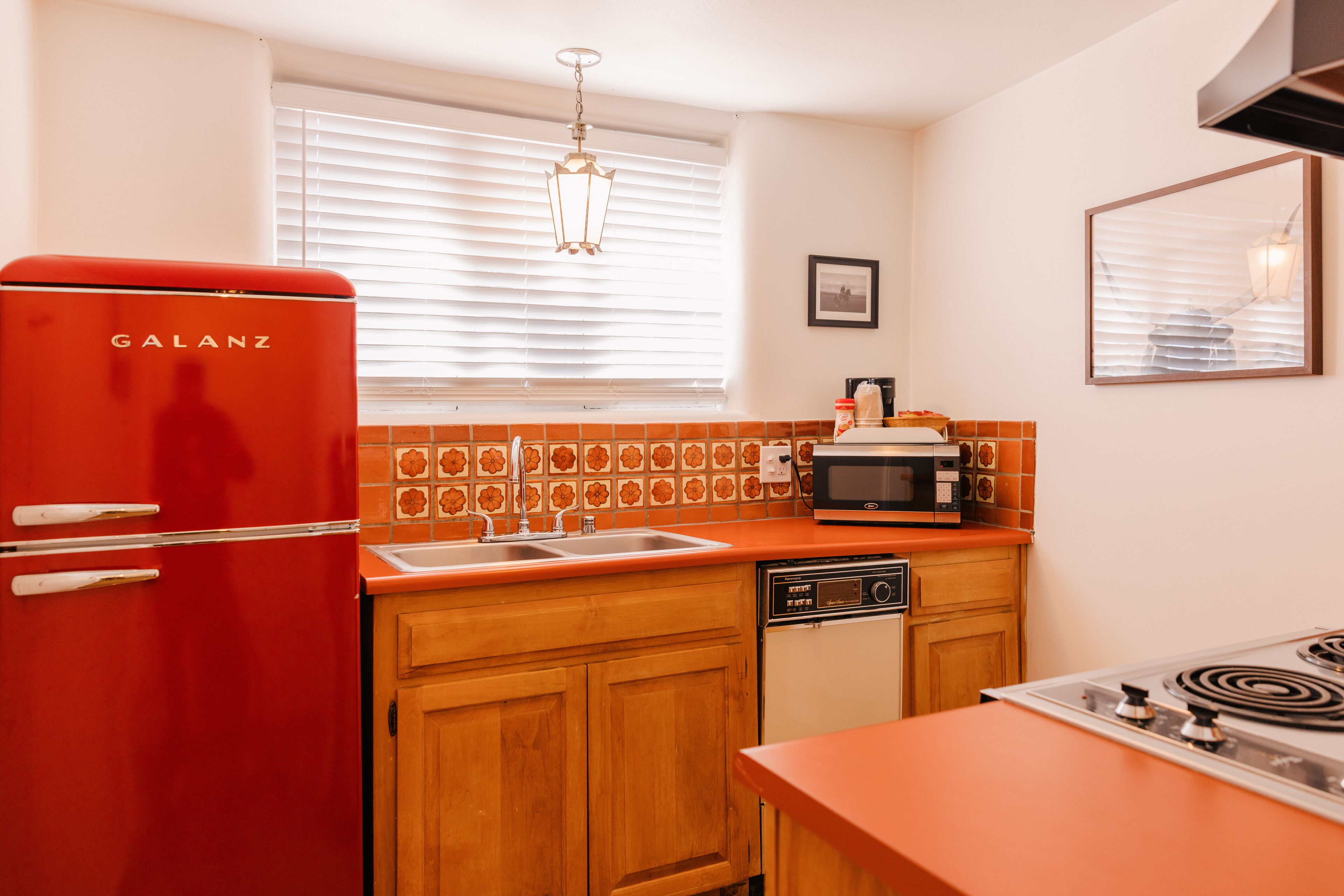 A kitchen with a red Galanz refrigerator, a microwave, a sink, wooden cabinets, and a stove.
