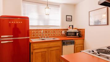 A kitchen with a red Galanz refrigerator, a microwave, a sink, wooden cabinets, and a stove.