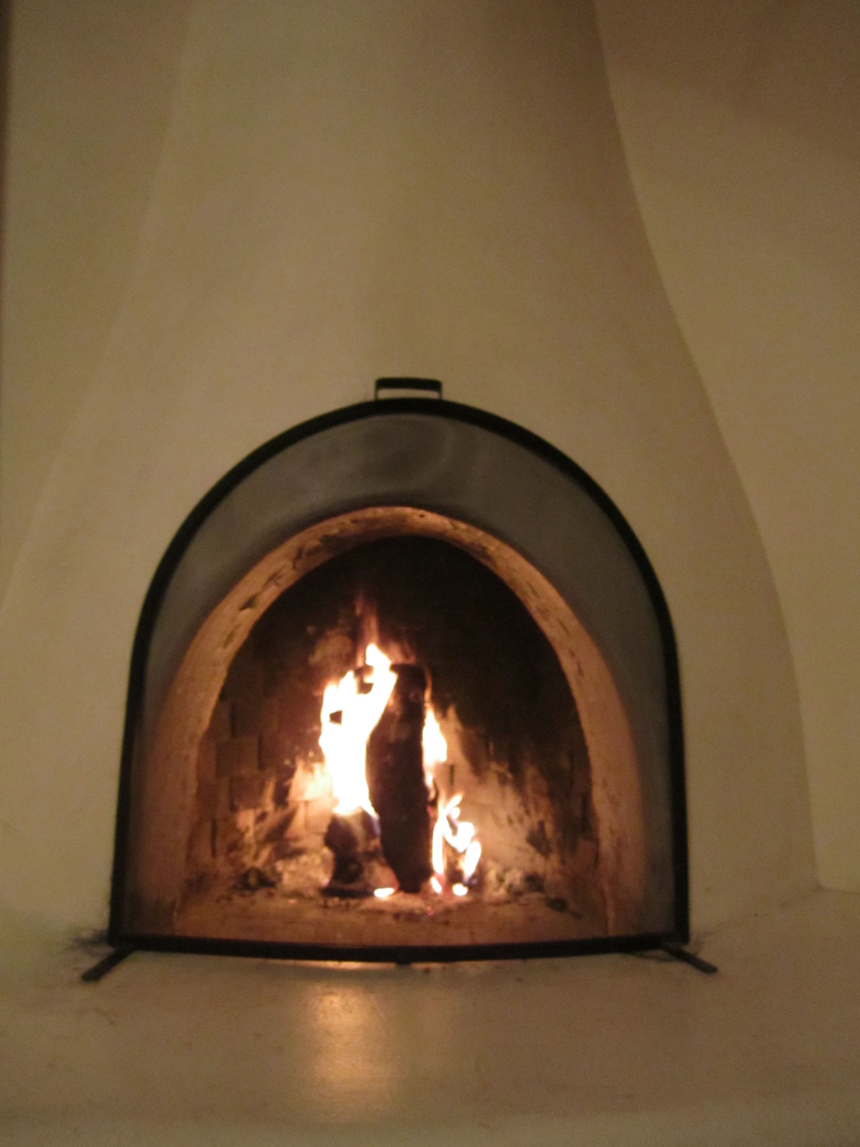 A stone fireplace with a fire burning inside, set in a white wall.