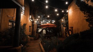 An outdoor patio area with string lights, a red umbrella, and a brick pathway. - Pueblo Bonito Inn (Santa Fe)