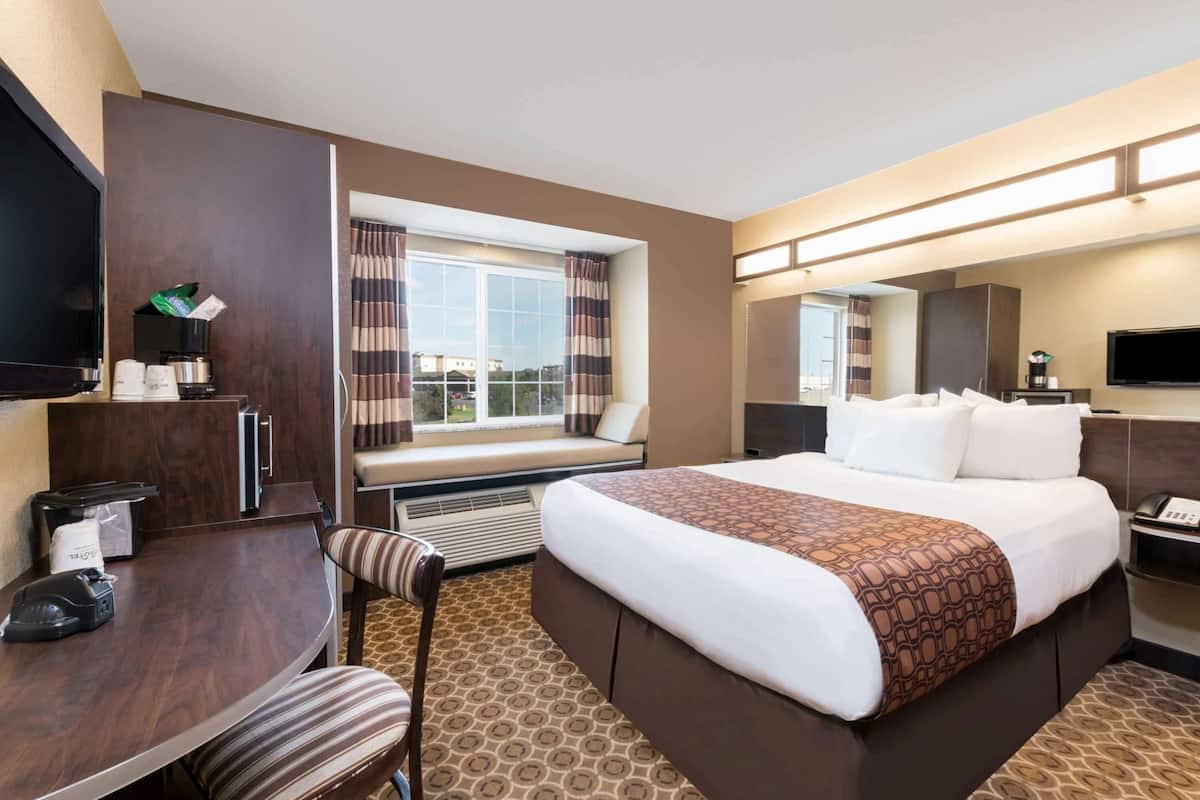 A hotel room with a large bed, a desk with a chair, a television, and a window with curtains.