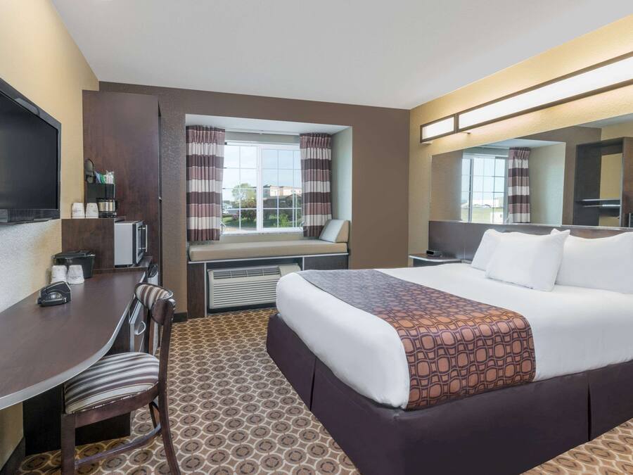 A hotel room with a large bed, a desk with a chair, a television, and a window with curtains.