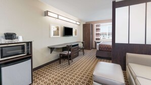 A hotel room with a kitchenette, a desk with two chairs, a bed, and a large window. - Microtel Inn & Suites by Wyndham Dickinson (Dickinson)