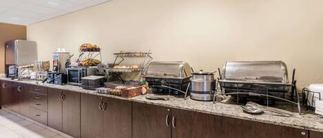 A buffet setup with various food stations, including a grill, a fruit display, and a beverage cooler.