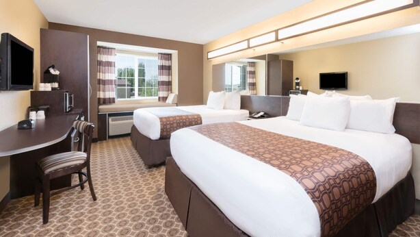 A hotel room with two beds, a desk, a chair, a TV, and a window with curtains. - Microtel Inn & Suites by Wyndham Dickinson (Dickinson)