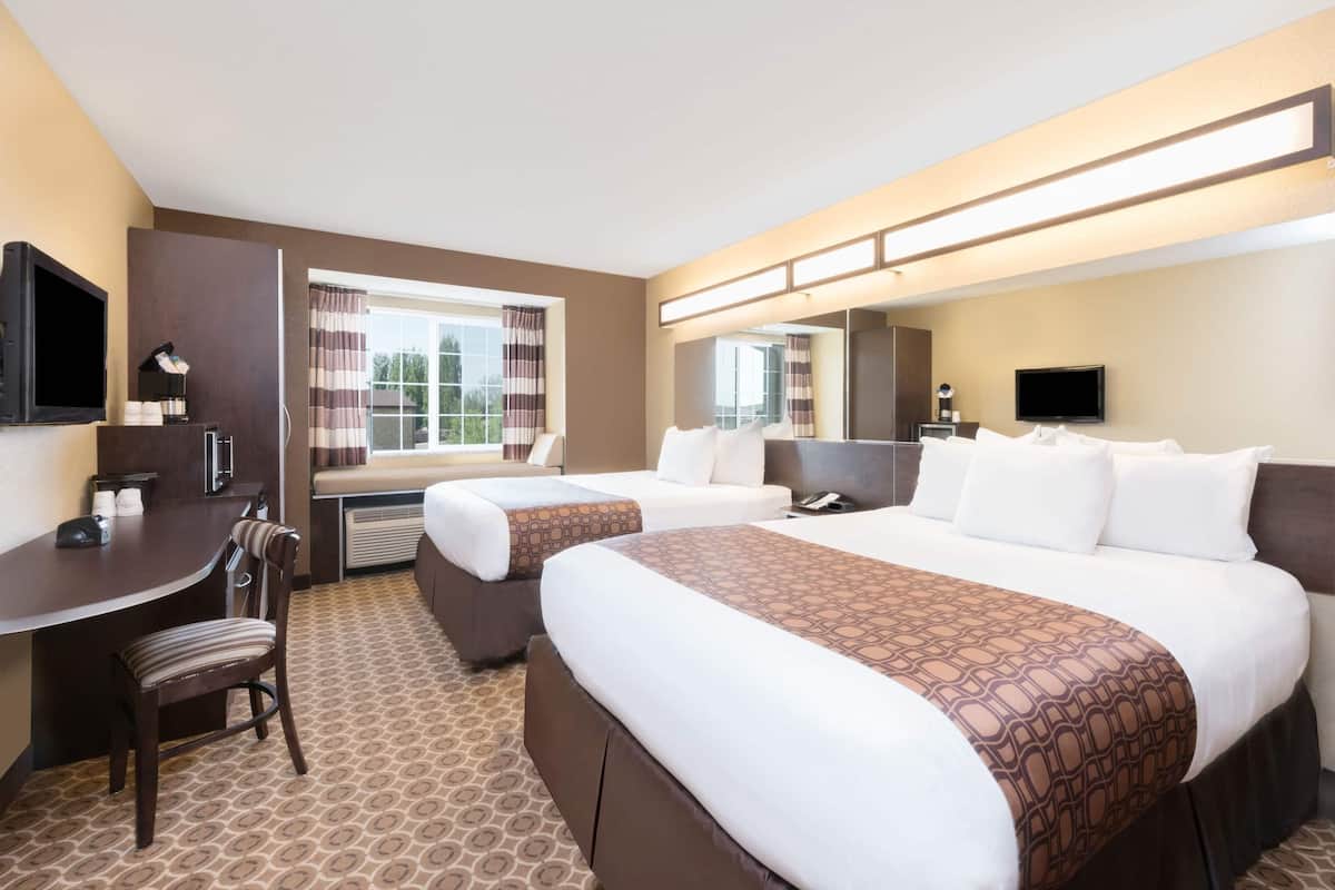 A hotel room with two beds, a desk, a chair, a TV, and a window with curtains.