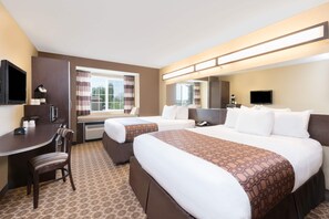 A hotel room with two beds, a desk, a chair, a TV, and a window with curtains. - Microtel Inn & Suites by Wyndham Dickinson (Dickinson)