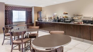 A hotel breakfast area with a buffet, seating, and a refrigerator. - Microtel Inn & Suites by Wyndham Dickinson (Dickinson)