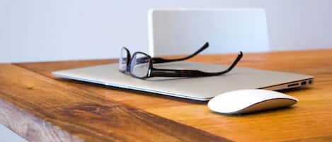 A laptop on a wooden table with a pair of glasses and a white mouse beside it.