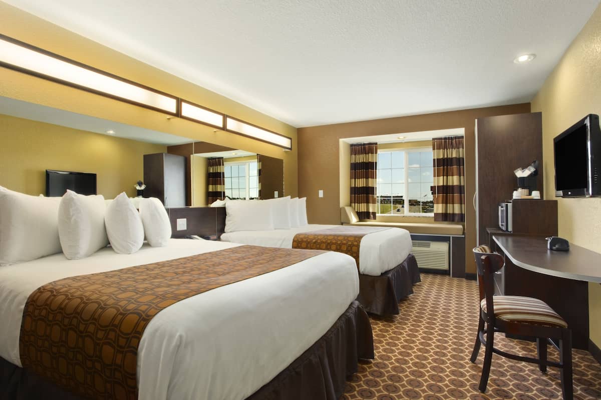 A hotel room with two beds, a desk, a chair, a TV, and a window with curtains.