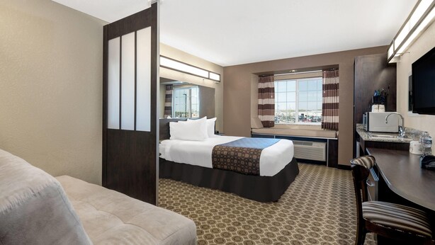 A hotel room with a bed, a desk, a chair, a window with curtains, and a view of the city. - Microtel Inn & Suites by Wyndham Williston (Williston)