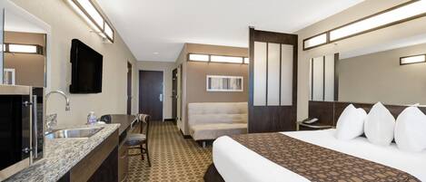 Habitació d'hotel amb un llit, una taula de nit amb un rentanet, una cadira, un mirall i una porta que condueix a una altra habitació.