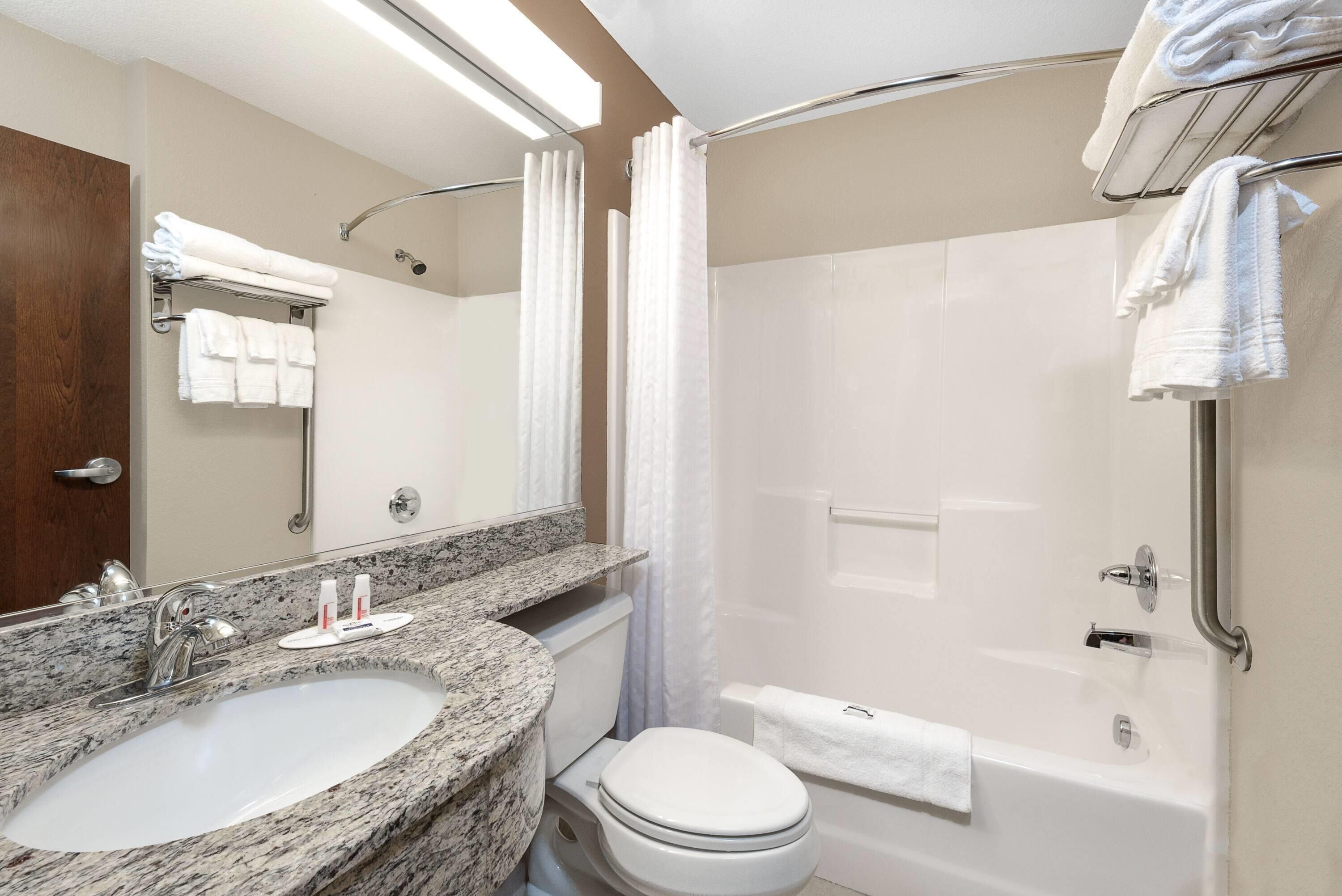 A bathroom with a granite countertop sink, a toilet, a bathtub, and a shower with a curtain.