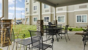 An outdoor patio with metal chairs and a table, a barbecue grill, and a stone pillar. - Microtel Inn & Suites by Wyndham Williston (Williston)
