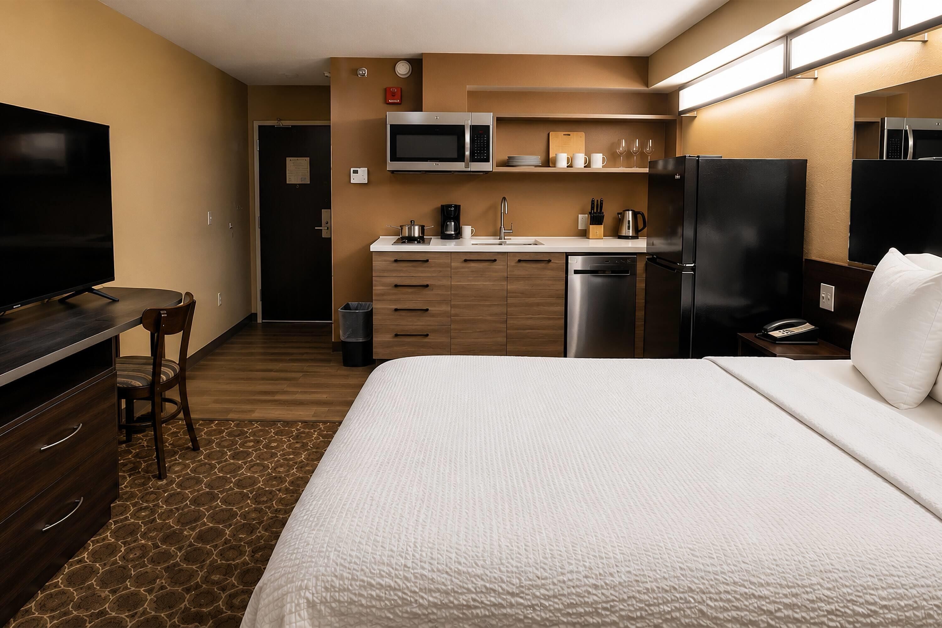 Une chambre d’hôtel équipée d’un lit, d’une télévision et d’une kitchenette avec un four à micro-ondes, un réfrigérateur et une machine à café.