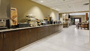 A hotel kitchen with a buffet setup, including a coffee machine, a food display, and a seating area with tables and chairs. - Microtel Inn & Suites by Wyndham Williston (Williston)