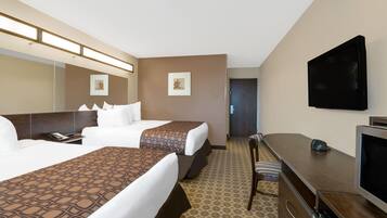 A hotel room with two beds, a desk, a television, and a door leading to another room.