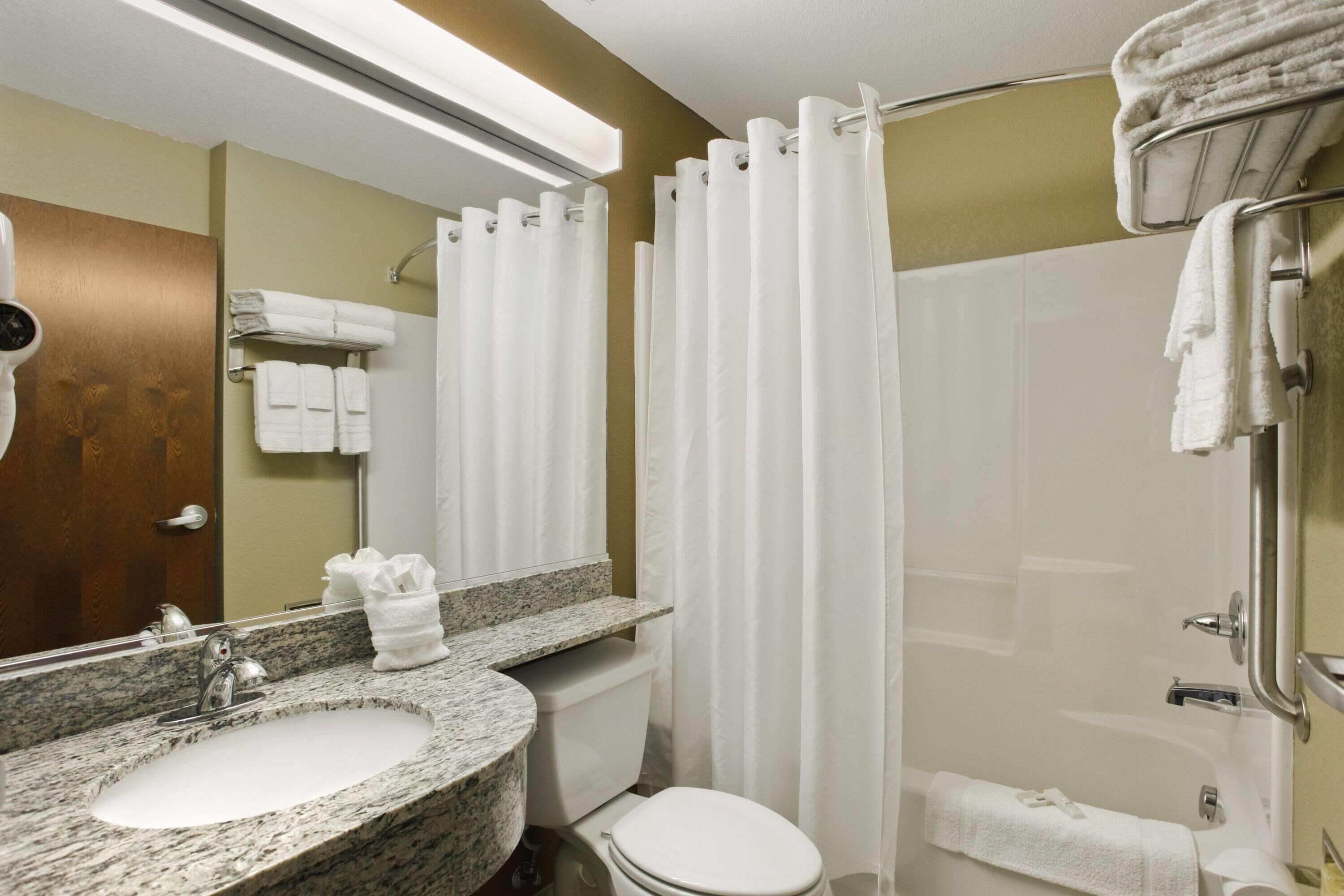 Un baño con lavamanos de granito, inodoro, ducha con cortina y toallero.