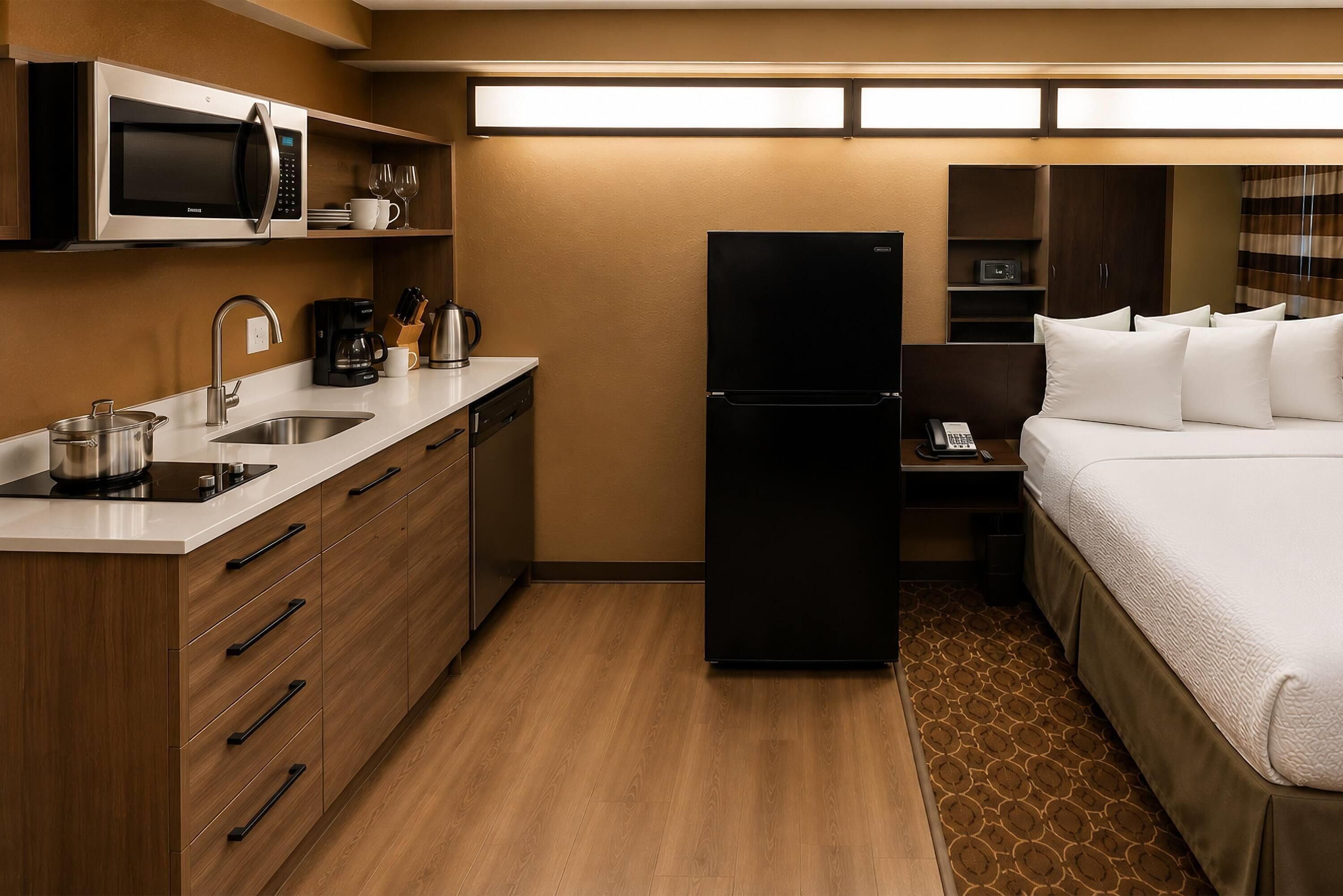 Een compacte hotelkamer met kitchenette, een bed, nachtkastje en een klein bureau.