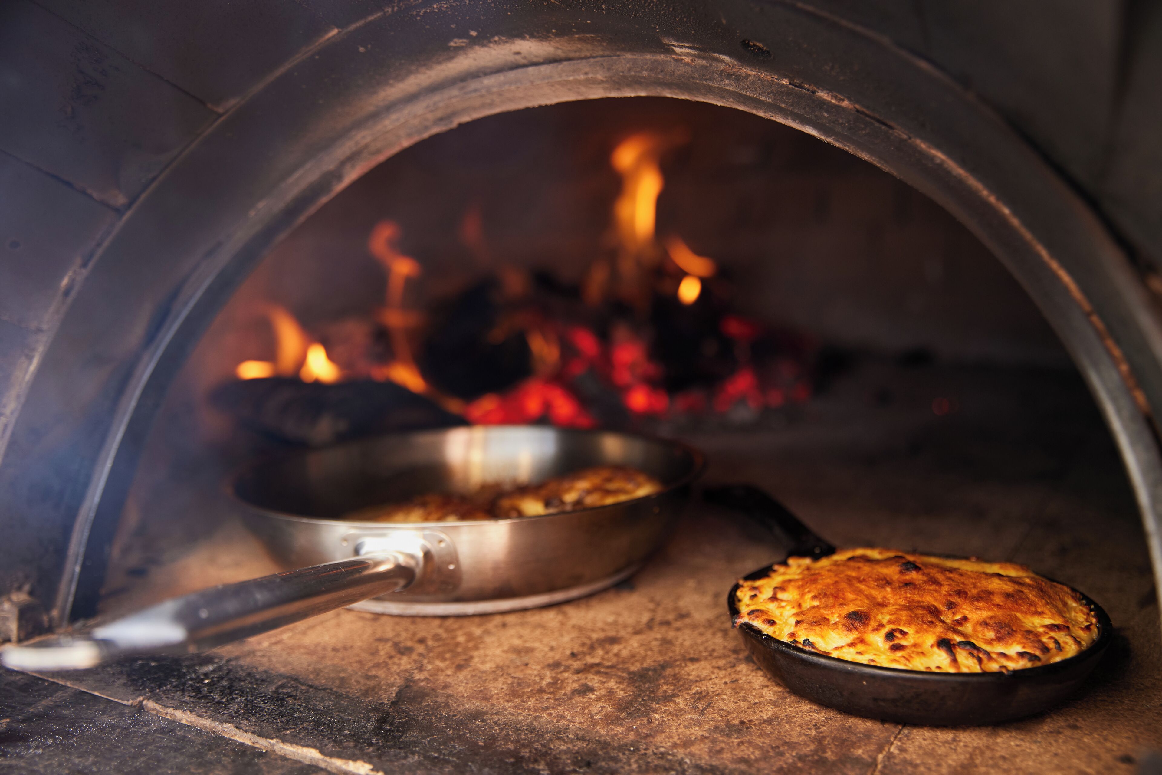 Un forno per pizza con una pizza all'interno, una pentola con cibo e fiamme sullo sfondo.