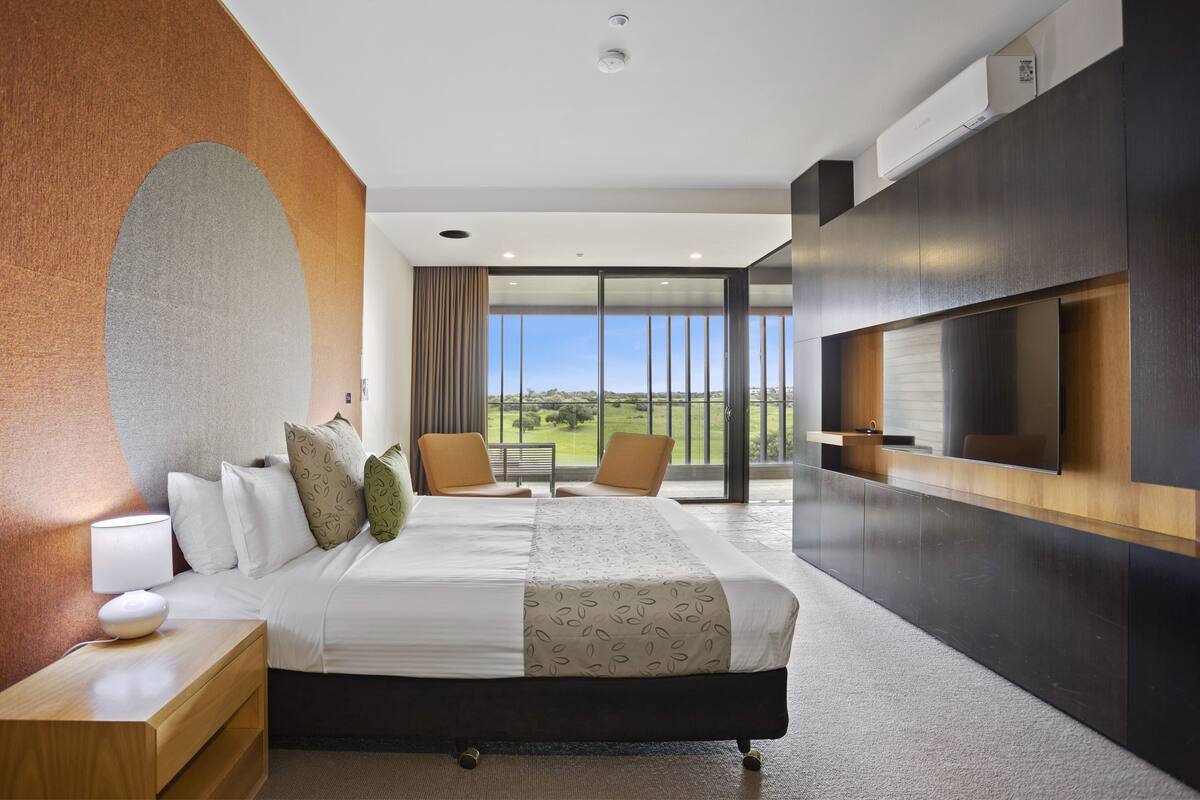 Ein modernes Hotelzimmer mit einem großen Bett, einem Fernseher und einem Balkon mit Blick auf die Landschaft.