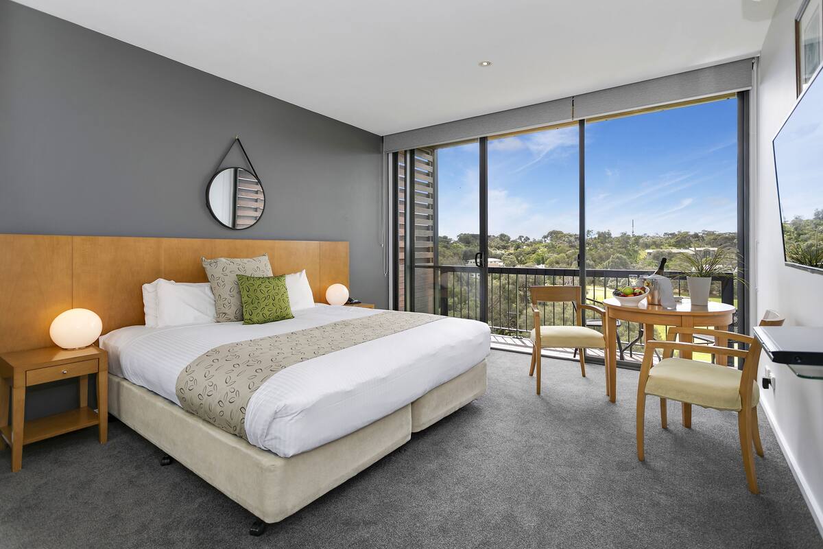 Ein modernes Hotelzimmer mit einem großen Bett, einem Schreibtisch und einem Balkon mit Blick auf die Stadt.