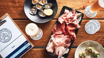 A wooden table with a menu, a plate of oysters, sliced meats, and a glass of beer.