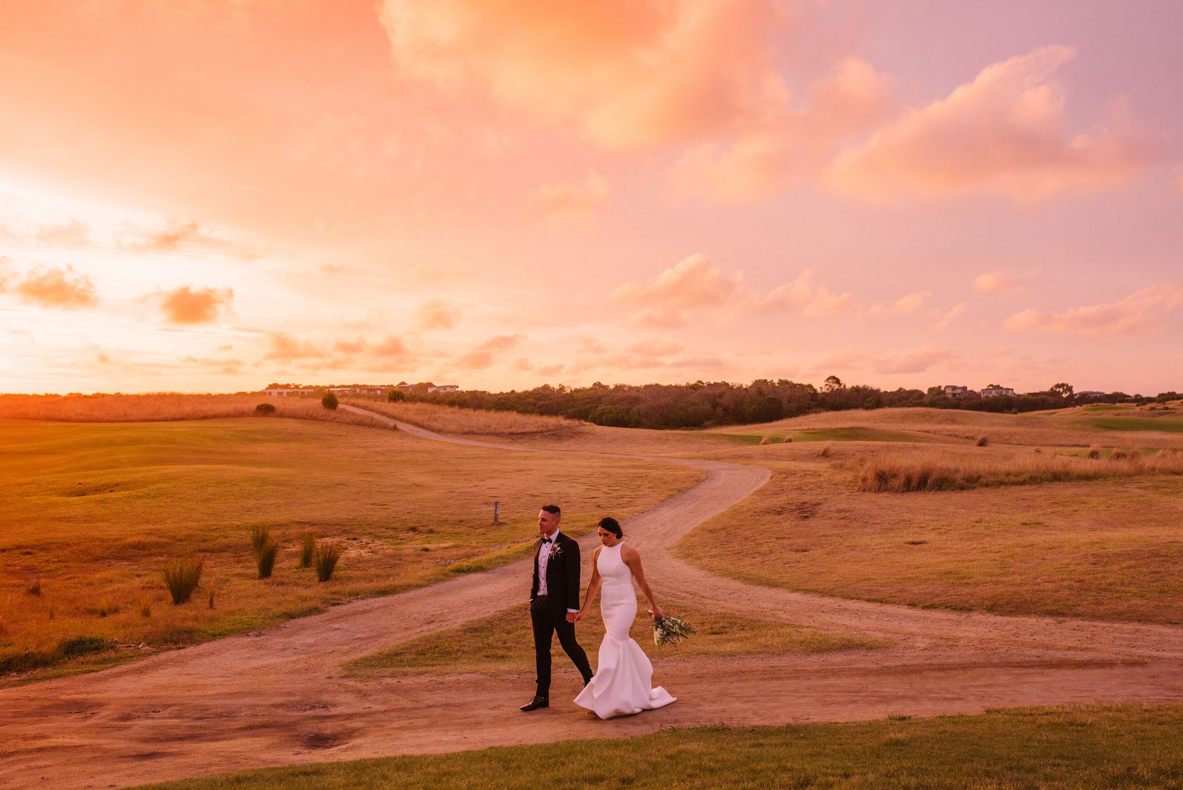 Una pareja caminando por un sendero de tierra en un campo con el atardecer de fondo.