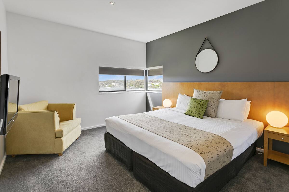 Ein modernes Hotelzimmer mit einem großen Bett, einer Couch, einem Fernseher und Blick ins Freie.