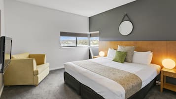 Een moderne hotelkamer met een groot bed, een bank, een televisie en uitzicht op het groen.