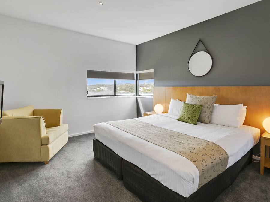 Een moderne hotelkamer met een groot bed, een bank, een televisie en uitzicht op het groen.