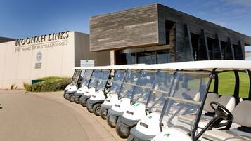 Un edificio con un cartel que dice "MOONAHI LINKS - THE HOME OF AUSTRALIAN GOLF" y una fila de carros de golf estacionados frente a él.