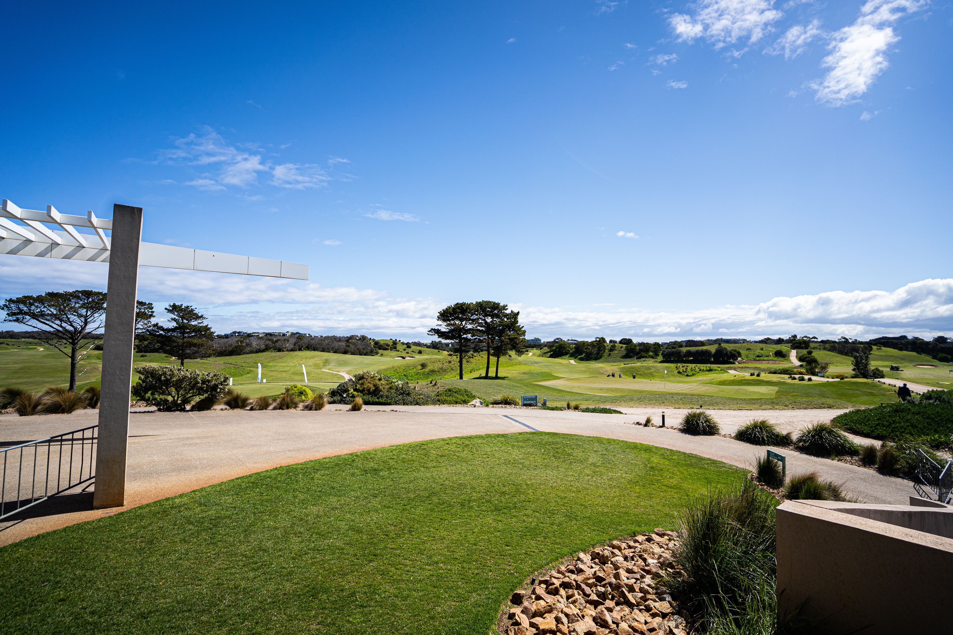 Um campo de golfe com céu claro, uma pérgula branca e um gramado bem cuidado.