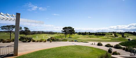 Um campo de golfe com céu claro, uma pérgula branca e um gramado bem cuidado.