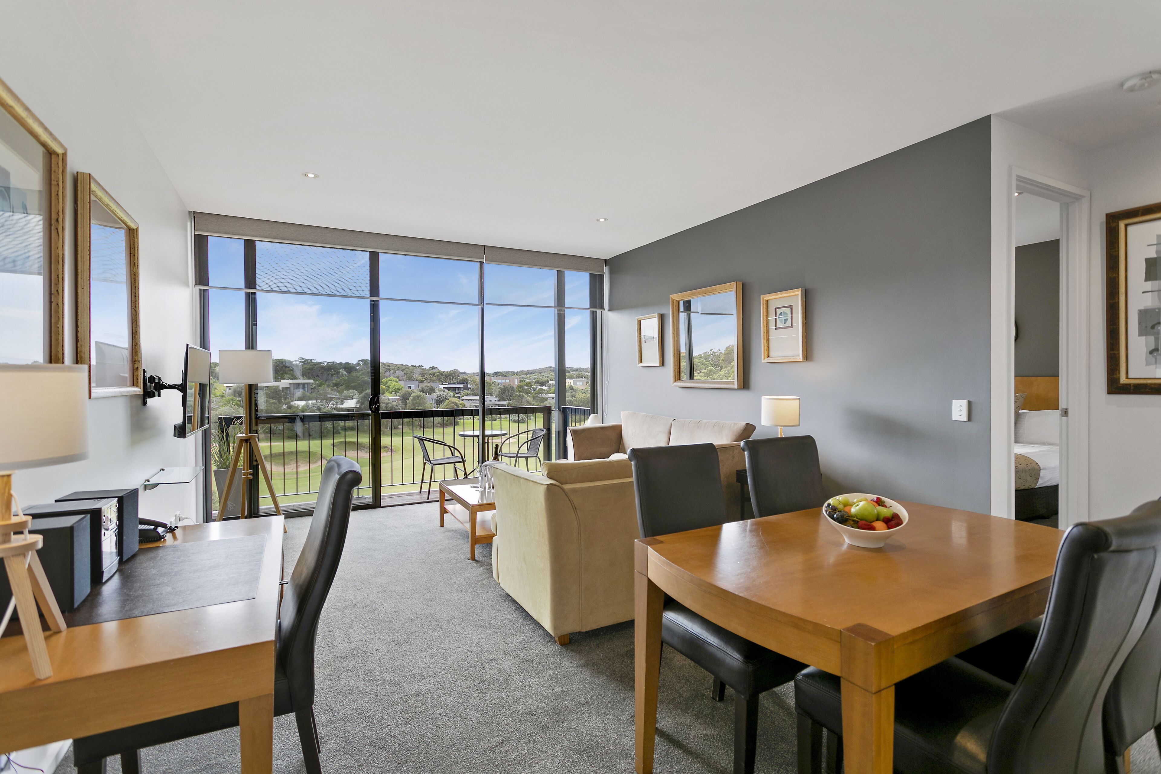 A modern hotel room with a balcony, a dining area, and a seating area.
