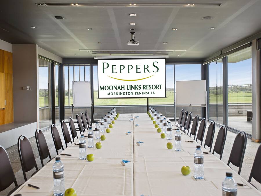 A conference room at Moonah Links Resort with a long table, chairs, water bottles, and apples.