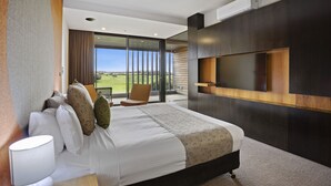Una habitación de hotel moderna con una cama grande, un televisor montado en la pared y un balcón con vistas al campo.