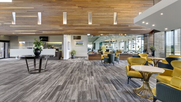 Un vestíbulo amplio con techo de madera, una mesa de recepción y zonas de estar amarillas.