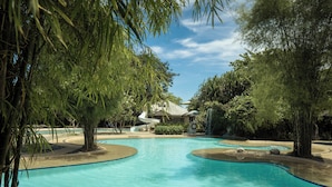 A pool area with a water slide, surrounded by trees and a building with a sloped roof. - Almont Inland Resort (Butuan)