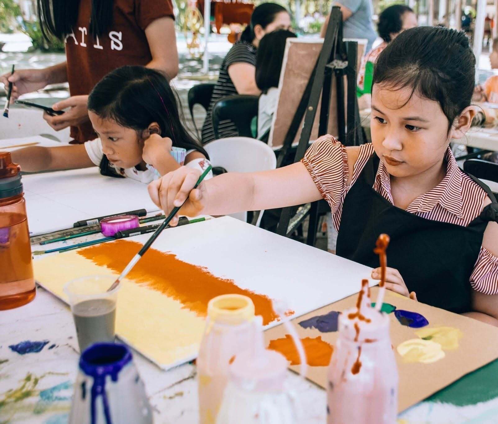 Children painting at a table with art supplies.