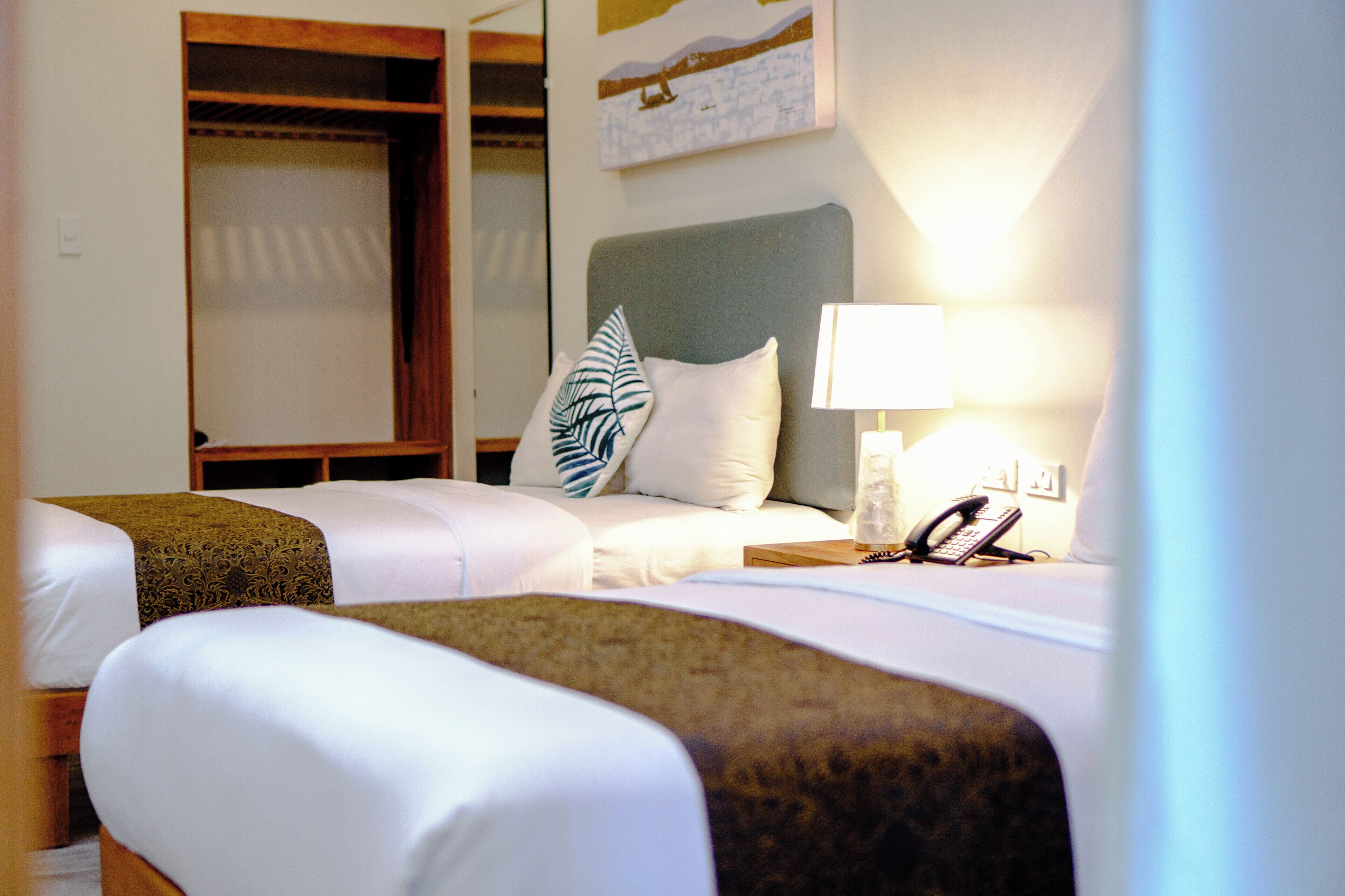 Quarto de hotel com duas camas, uma luminária, um telefone e um quadro na parede.