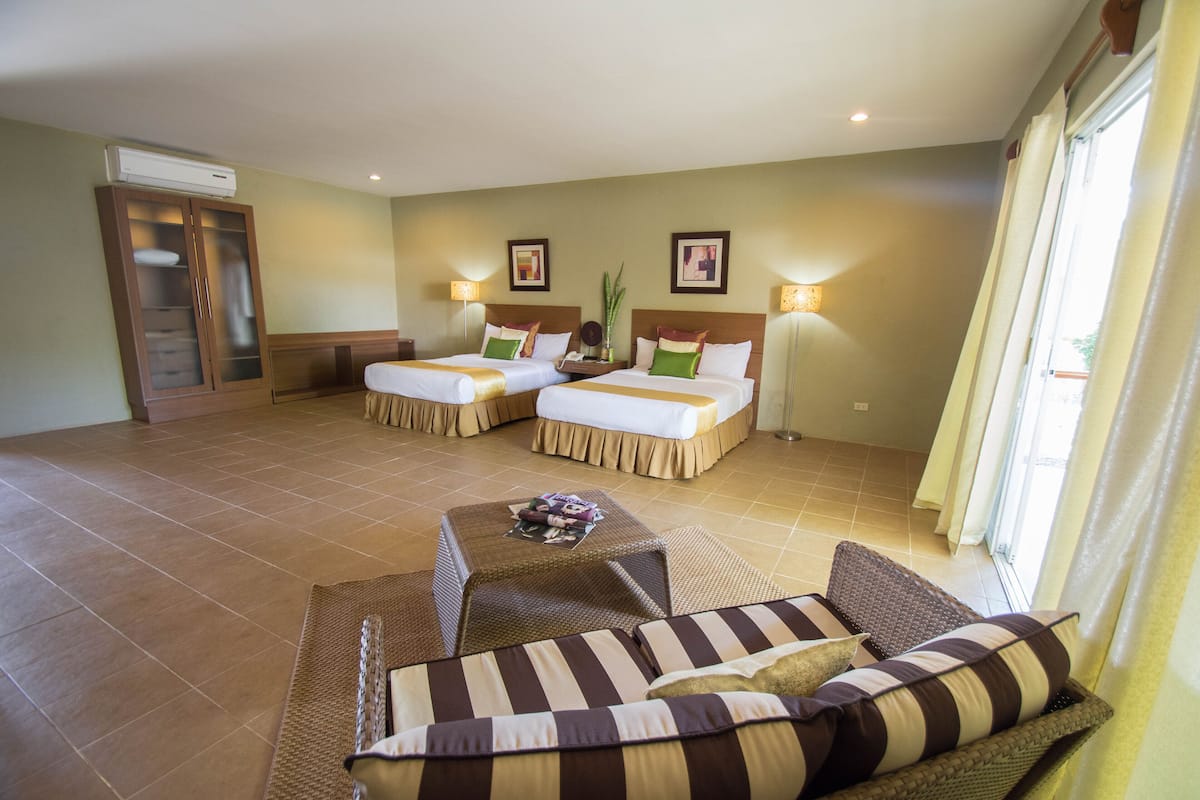 A hotel room with two beds, a sofa, a small table, and a cabinet.