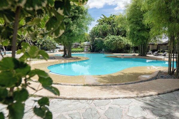 A swimming pool with a stone border, surrounded by trees and lounge chairs.