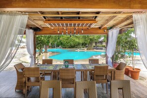 Zona d'estar a l'aire lliure amb mobiliari de vimetla, una piscina i plantes en testos.