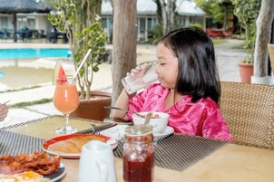 Un comedor con vista a la piscina, muebles de mimbre y una mesa con alimentos para el desayuno.