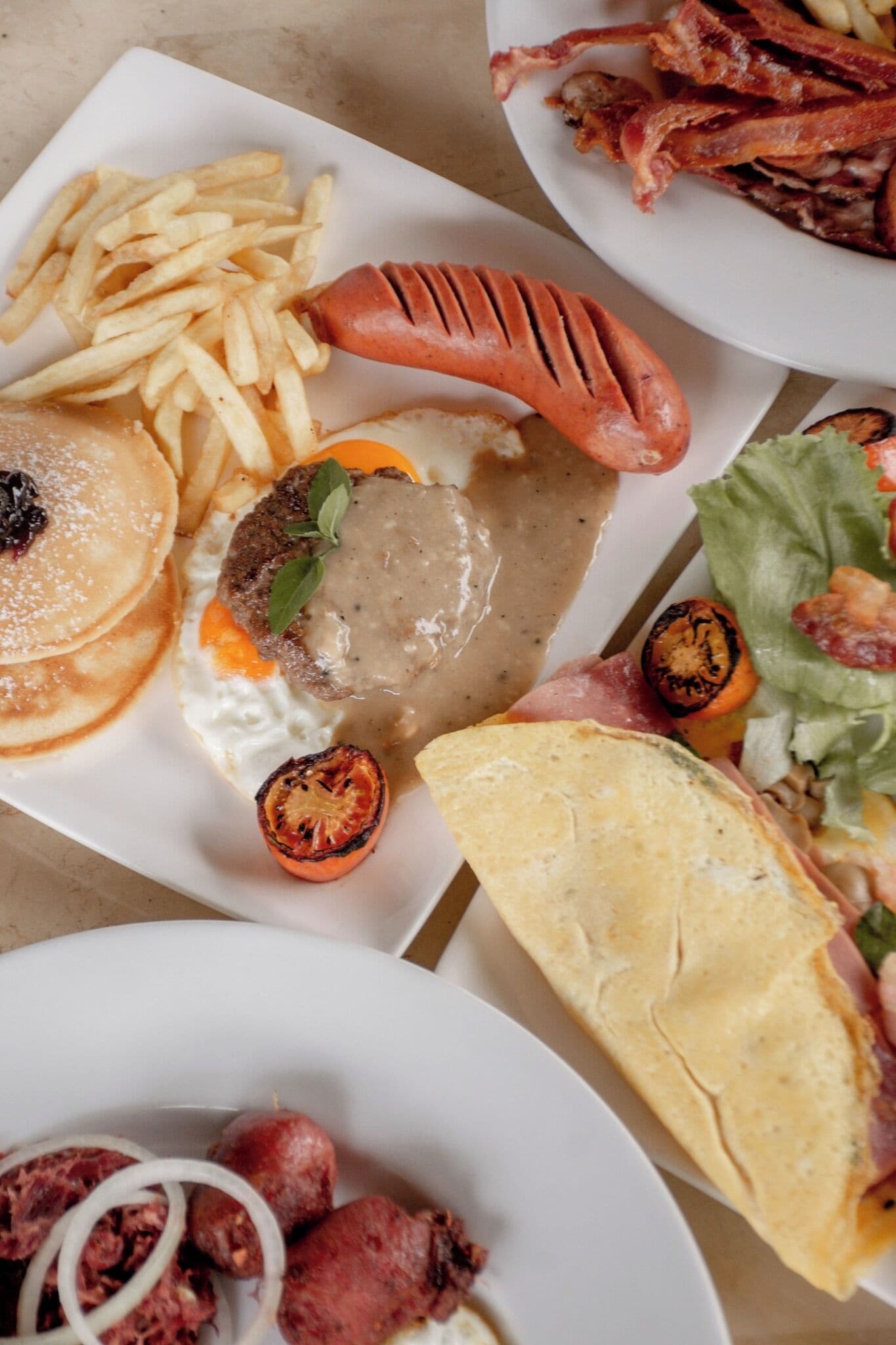 A variety of dishes including pancakes, sausages, and grilled vegetables on a table.