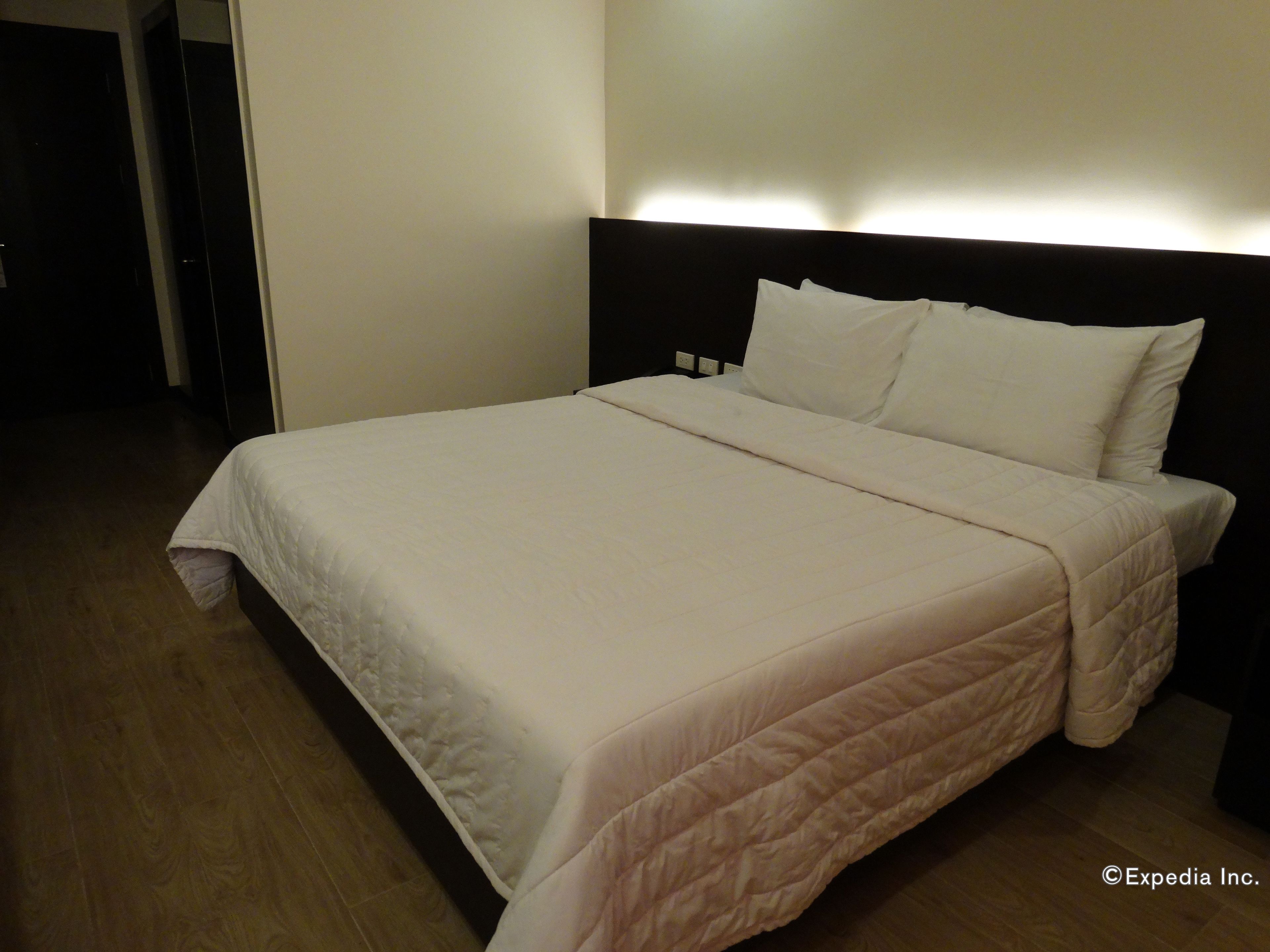 A neatly made bed with a white duvet and pillows, a dark headboard, and a wooden floor.