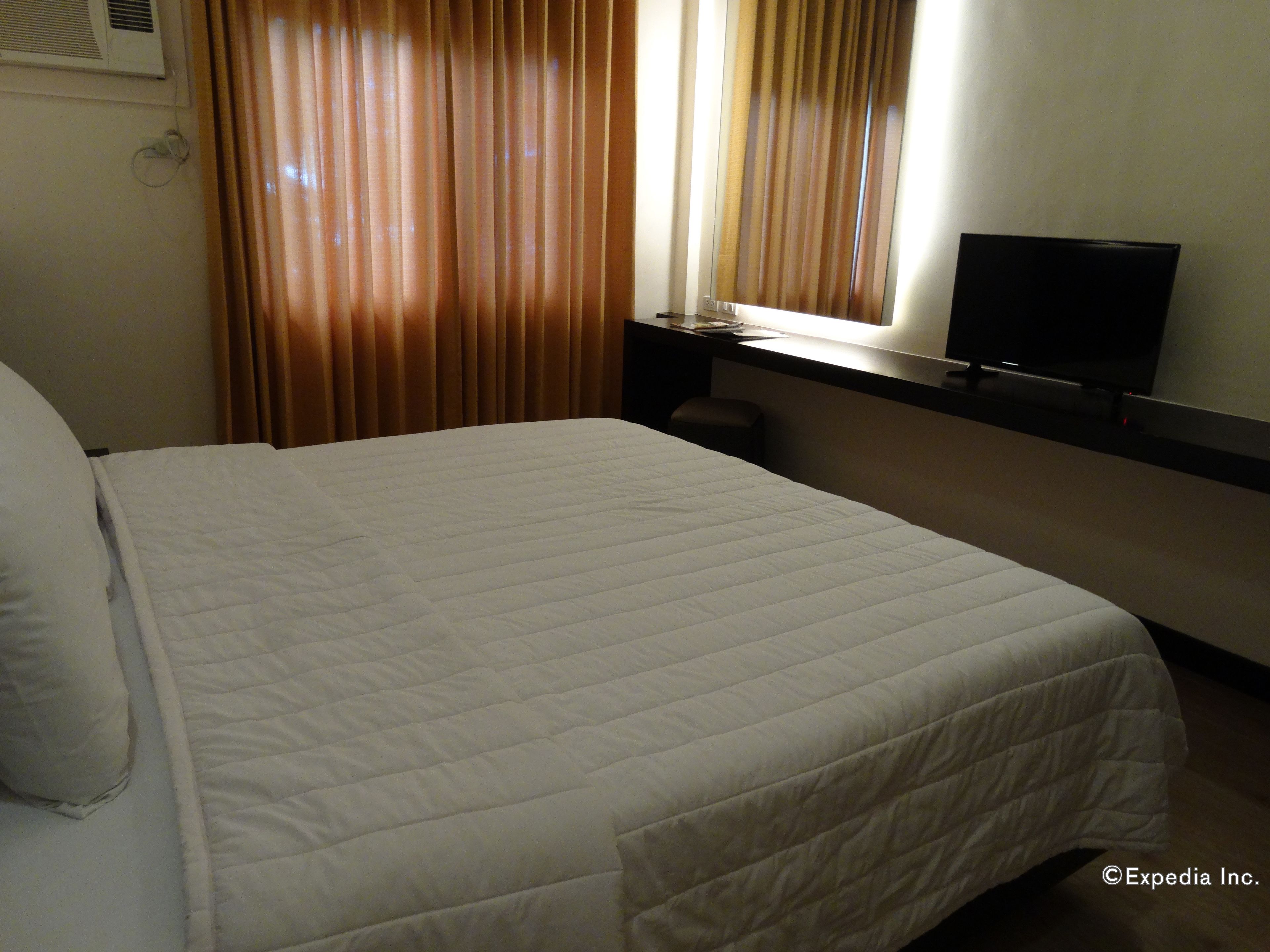 Una habitación de hotel con una cama grande, un televisor sobre un mueble y una ventana con cortinas.