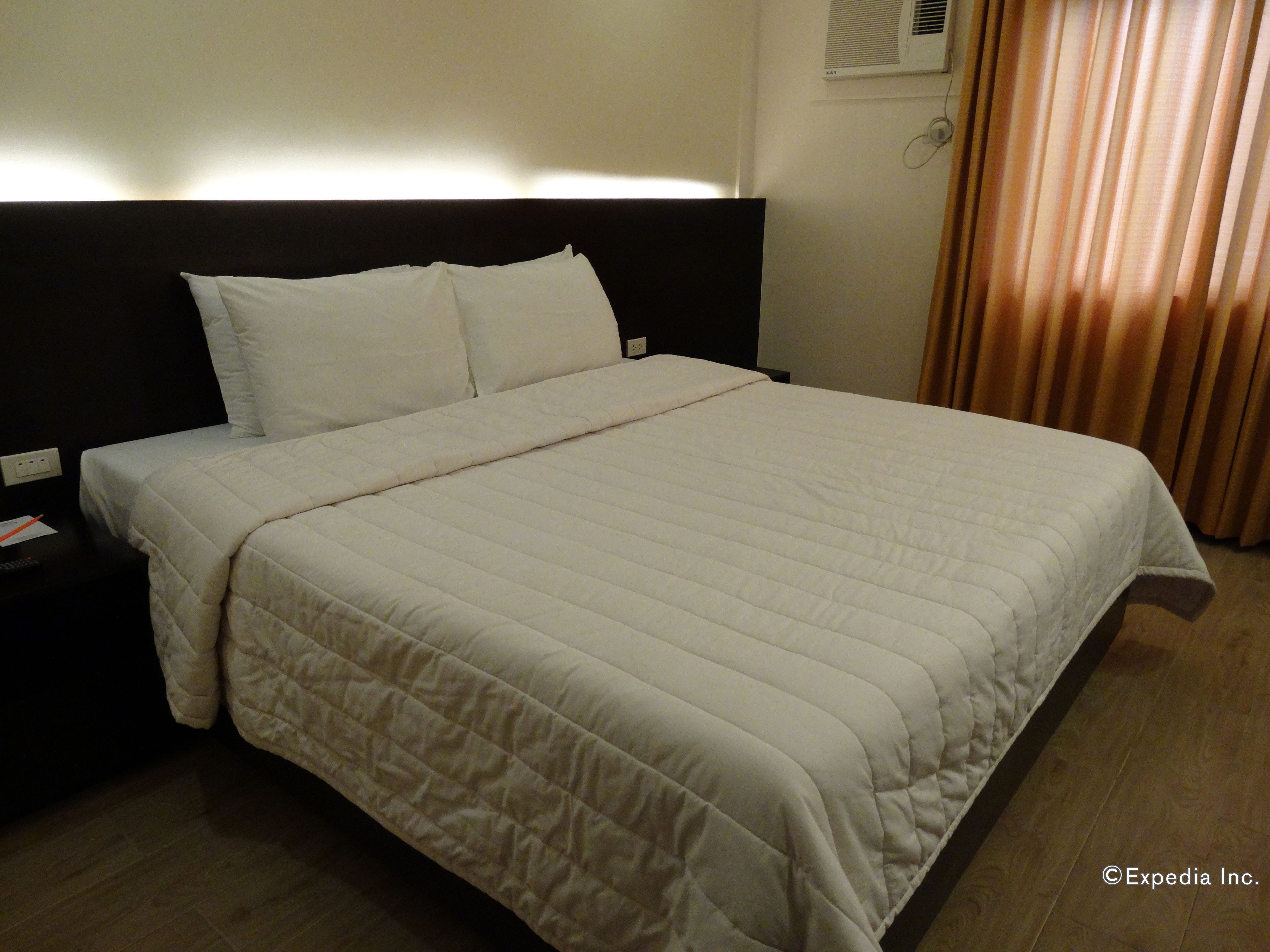 A hotel room with a large bed, a black headboard, white bedding, and a wooden floor.